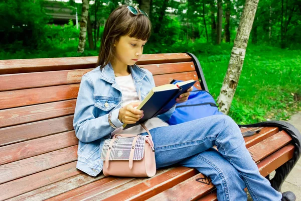 Menina estudante bonita e feliz sentada no banco, com as mãos em pilha de livros, olhando para a câmera e sorrindo. Verão ou primavera parque verde no fundo — Fotografia de Stock