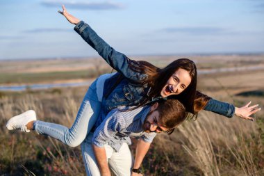 Kot pantolonlu kadın erkeklerin sırtına atladı ve mutlu oldular ve gökyüzüyle çimen tarlasında güldüler.