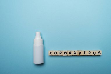 Beyaz şişe el dezenfektanı, üzerinde Coronavirus kelimesi yazılı, ahşap blokta mavi arka planda izole edilmiş. Virüs salgını önleme kavramı.
