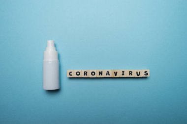 Beyaz şişe el dezenfektanı, üzerinde Coronavirus kelimesi yazılı, ahşap blokta mavi arka planda izole edilmiş. Virüs salgını önleme kavramı.
