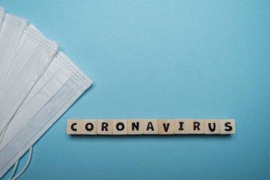 Mavi arka planda tahtadan bloğa yazılmış Coronavirus kelimesiyle hijyenik yüz maskesi. Virüs salgını önleme kavramı.