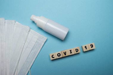 Hijyenik yüz maskesi ve beyaz şişe el dezenfektanı. Mavi arka planda ahşap blokta yazılı. Virüs salgını önleme kavramı.