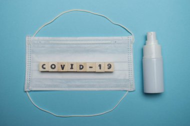 Hijyenik yüz maskesi ve beyaz şişe el dezenfektanı. Mavi arka planda ahşap blokta yazılı. Virüs salgını önleme kavramı.