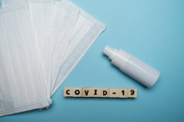Hijyenik yüz maskesi ve beyaz şişe el dezenfektanı. Mavi arka planda ahşap blokta yazılı. Virüs salgını önleme kavramı.