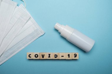 Hijyenik yüz maskesi ve beyaz şişe el dezenfektanı. Mavi arka planda ahşap blokta yazılı. Virüs salgını önleme kavramı.