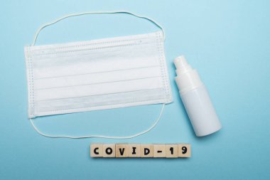 Hijyenik yüz maskesi ve beyaz şişe el dezenfektanı. Mavi arka planda ahşap blokta yazılı. Virüs salgını önleme kavramı.