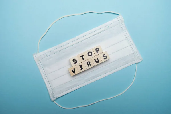 Hygienic face mask with stop virus word written on wood block isolated over blue background. Virus outbreak prevention concept.