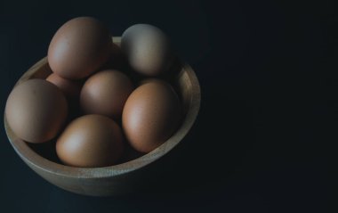 Siyah arka planda ahşap bir kasede tavuk yumurtası.