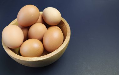 Siyah arka planda ahşap bir kasede tavuk yumurtası.