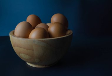 Siyah arka planda ahşap bir kasede tavuk yumurtası.