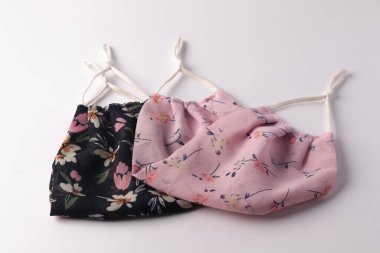 Beyaz bir yüzeyde iki parçalı kumaş maskesi ve bir parça kumaş, antivirüs ve koronavirüs maskesi (COVID-19) pamuktan yapılmıştır..