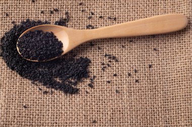 Kahverengi bir kumaş üzerinde tahta kaşıkta siyah susam tohumları.