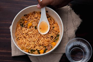 Tom, ahşap zeminde beyaz bir seramik bardakta hazır şehriye yiyor.