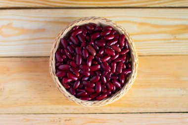 Ahşap bir zeminde hasır sepetteki kırmızı fasulyeler.