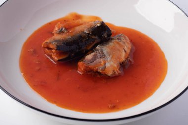 Beyaz arka planda beyaz tabakta domates soslu sardalyalar.