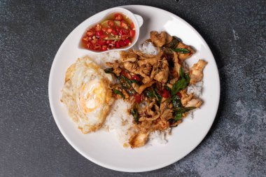 Tavuklu fesleğen pilavı ve siyah arka planda beyaz tabakta kızarmış yumurta..