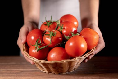 Kahverengi dokuma sepeti taze toplanmış kırmızı domateslerle dolu. Beyaz takım elbiseli biri tarafından tutulmuş.