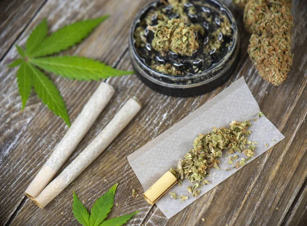 Cannabis joints with rolling paper and grinder over wood background