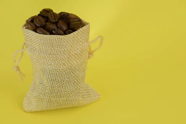 Malý sáček s kávovými zrny stojí vzpřímeně na žlutém pozadí — Stock fotografie
