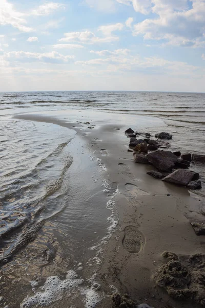 Impronte su scarpe su sabbia bagnata vicino a un mucchio di pietre sulla riva del mare contro un cielo nuvoloso — Foto Stock