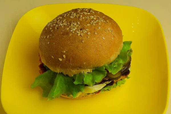 En una placa de cerámica amarilla se encuentra un gran sándwich. Placa de tiro de cerca en una mesa de madera beige — Foto de Stock