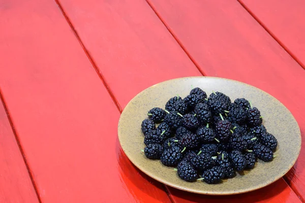 A plate with mulberry stands on a bright red wooden table to the left Stock Image