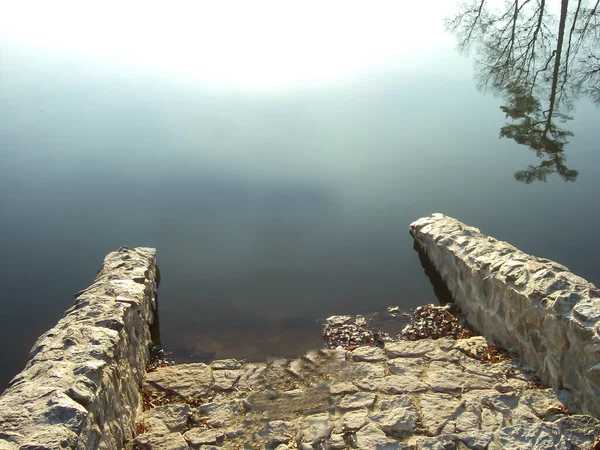 Batu langkah-langkah pada tanggul turun ke dalam air, yang mencerminkan matahari — Stok Foto