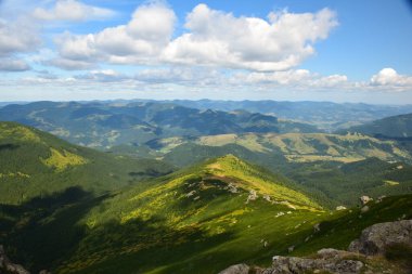 Dağlar arasındaki vadi güneş ışığıyla yıkanır ve dağlar ağaçlarla kaplıdır. Mavi gökyüzünde küçük bulutlar
