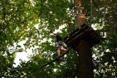 Genç adam halat parkında ağaçtan ağaca koşuyor.