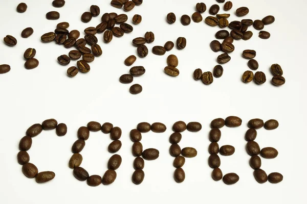 Das Wort KAFFEE ist auf weißem Hintergrund mit Kaffeebohnen ausgelegt. Kaffeebohnen sind oben verstreut — Stockfoto