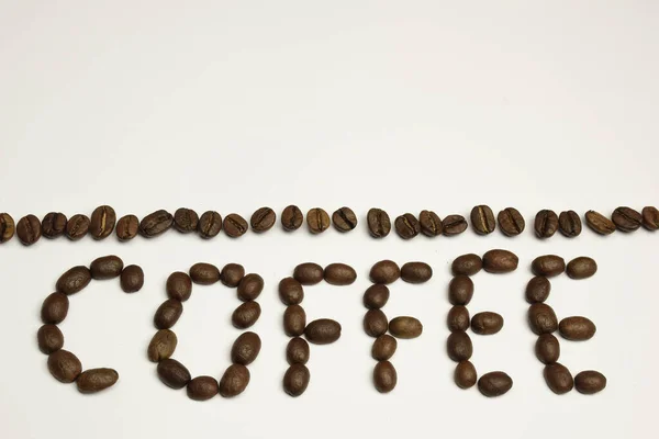 Слово COFFEE выложено на белом фоне с кофейными зёрнами. Над ним полоска кофейных зерен — стоковое фото