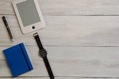 Bir e-kitap, bir kol saati, bir günlük ve bir kalem bej bir tahta masanın üzerinde yatıyor. Fotoğrafın sağında boş bir alan var.