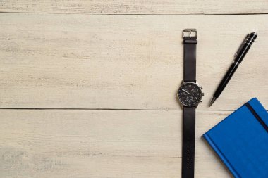 Mekanik bir kol saati, bir günlük ve bir kalem sağ tarafta, tahta bir masanın üzerinde.