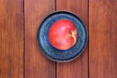 Ahşap bir arka planda, seramik bir tabağın üzerinde kırmızı bir elma yatıyor. Çerçevenin ortasında.