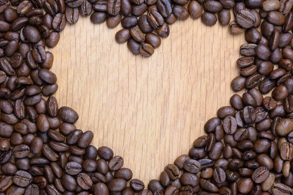 Srdce je umístěno na dřevěném povrchu z kávových zrn. Ve středu je mezera pro nápis. — Stock fotografie