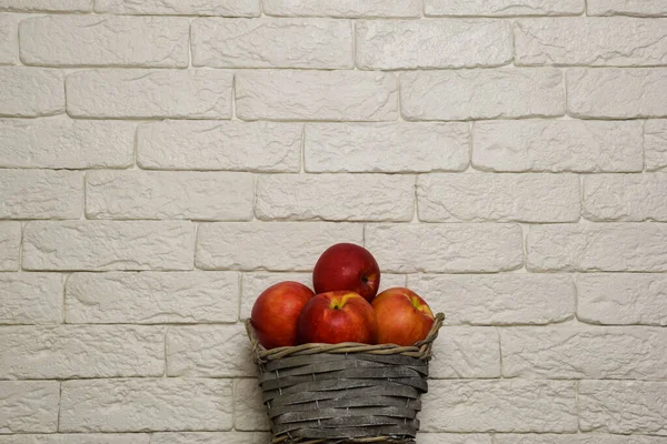 Корзина с красными яблоками на фоне кирпичной стены. Корзина находится в нижнем центре рамы. Вверху есть место для надписи — стоковое фото