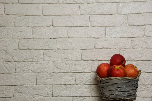 Cesta con manzanas rojas sobre un fondo de una pared de ladrillo claro. La cesta está en la parte inferior a la derecha del marco. Hay un lugar para una inscripción en la parte superior — Foto de Stock