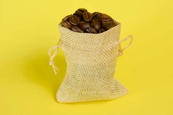 Malý ozdobný pytel z konopné tkaniny s kávovými zrny na jasně žlutém pozadí — Stock fotografie