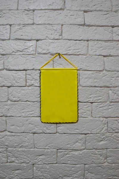 一根黄色的旗子挂在浅色的砖墙上 旗子是干净的 没有题词或图画 四周环绕着黄黑相间的边界 — 图库照片