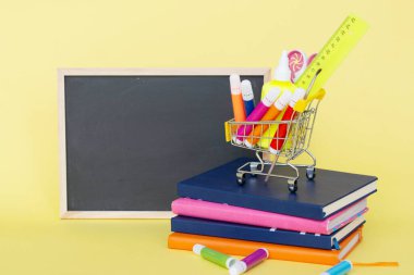Sarı kağıt arka plandaki okul konseptine geri dönelim. Kırtasiyeli sepet. Kitaplar. tahtada.