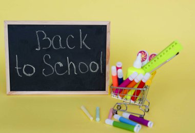 Sarı kağıt arka plandaki okul konseptine geri dönelim. Kırtasiyeli sepet. Kitaplar. tahtada.