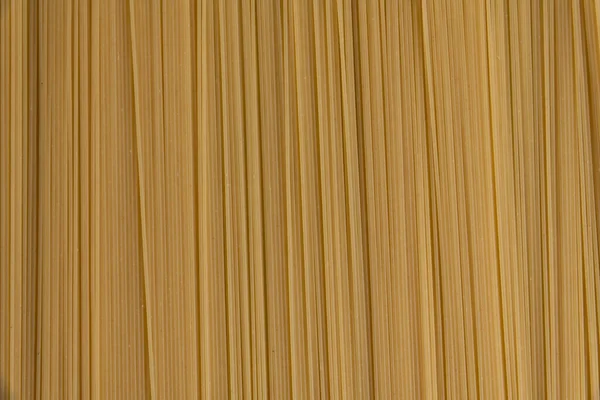 Abstract textured food background of raw uncooked spaghetti pasta made from milled durum wheat. Top down view. Copy space for your text. Italian cuisine theme.