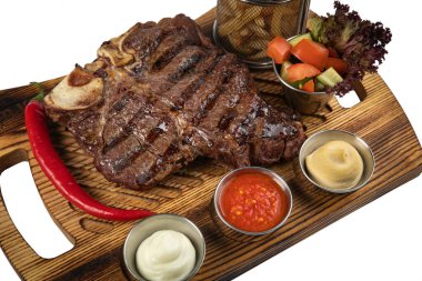 grilled steak on a wooden board with tomatoes, sauces, french fries and spices