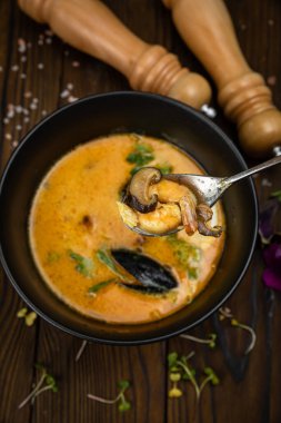 Thai spicy seafood soup in dark plate on wooden background