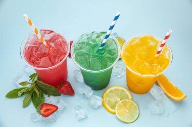 mavi arka planda buzlu, meyveli ve meyveli plastik bardaklarda renkli limonatalar.