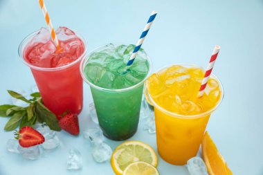 mavi arka planda buzlu, meyveli ve meyveli plastik bardaklarda renkli limonatalar.