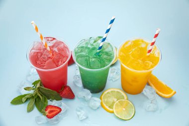 mavi arka planda buzlu, meyveli ve meyveli plastik bardaklarda renkli limonatalar.