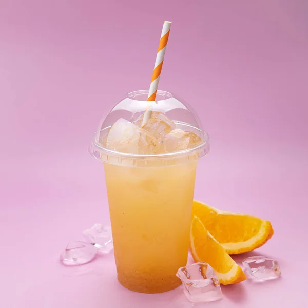 Yaz İçeceği Taze Limonata. Pembe arka planda, plastik bardakta turuncu.