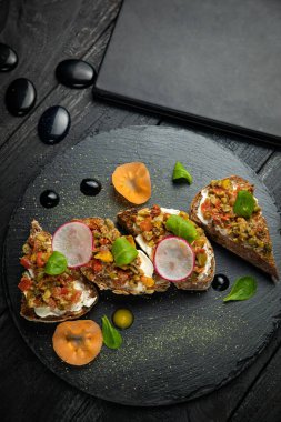 Vejetaryen bruschettalar, peynirli, sebzeli, siyah bir taş tahtada.