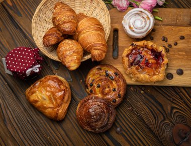 Çeşitli hamur işleri, kruvasanlar, çörekler. Kahverengi ahşap masada.
